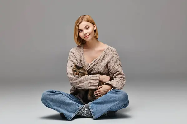 短い髪の魅力的な女性が床に座り 穏やかに彼女の膝に猫を抱き 自宅で平和な瞬間を楽しんでいる — ストック写真