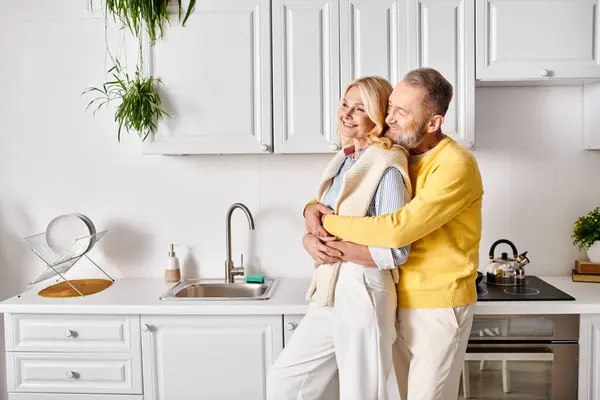 居心地の良い家庭用ウェアの成熟した男女 居心地の良いキッチンセッティングで愛するハグを共有 — ストック写真