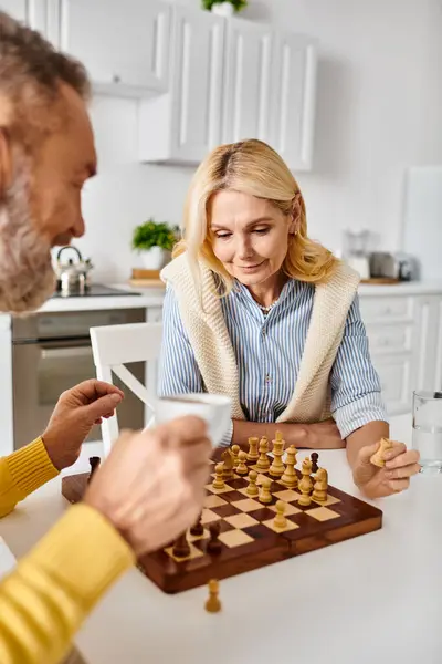 stock image A mature loving couple in cozy homewear engrossed in a game of chess, strategizing and contemplating their moves.