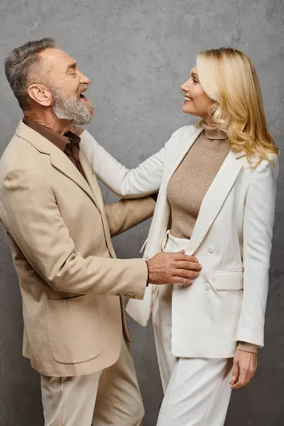 stock image A mature man and woman in debonair attire stand side by side, exuding love and grace against a gray backdrop.