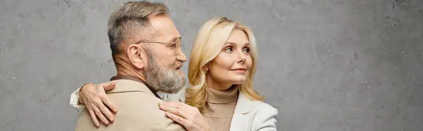 stock image A mature man and woman in debonair attire embracing each other with love and grace against a gray backdrop.