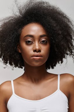 Şehvetli afro saçlı şık bir Afrikalı Amerikalı kadın stüdyo ortamında kendine güvenen bir poz veriyor..