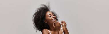 Kıvırcık saçlı, stüdyo ortamında bikini giyen Afro-Amerikan bir kadın..