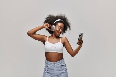 Beyaz bluzlu Afro-Amerikan bir kadın zarif bir şekilde cep telefonu tutuyor..