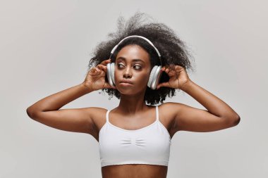 Kıvırcık saçlı genç bir Afrikalı Amerikalı kadın kulaklıkla müzik dinliyor..