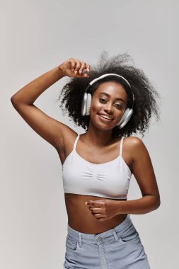 Güzel, kıvırcık saçlı, kulaklık takan ve beyaz bluzlu Afro-Amerikan bir kadın..