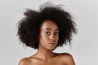 Kıvırcık saçlı genç bir Afrikalı Amerikalı kadın stüdyo ortamında şık bir poz veriyor..