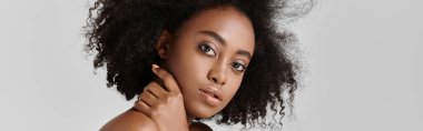 Kıvırcık saçlı Afro-Amerikan bir kadın stüdyo ortamında poz veriyor..