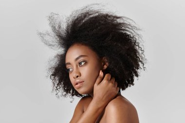 Kıvırcık saçlı, güzel bir Afro-Amerikan kadın stüdyoda kendine güvenerek poz veriyor..