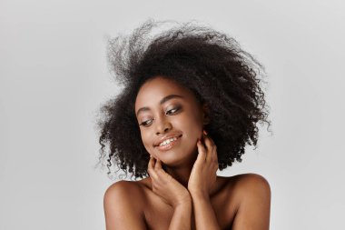 Afro saçlı, kıvırcık saçlı, güzel bir Afrikalı Amerikalı kadın stüdyo ortamında kendine güvenen bir poz veriyor..