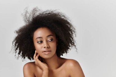 Çekici bir Afrikalı Amerikalı kadın kıvırcık saçlı stüdyo ortamında poz veriyor..