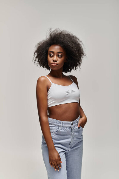A stylish African American woman confidently rocks a crop top and jeans, showcasing her trendy and casual fashion sense.