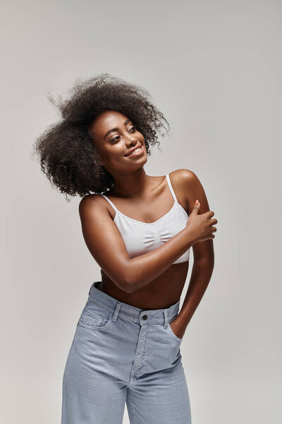 A beautiful young African American woman with curly hair poses confidently for a picture in a studio setting.