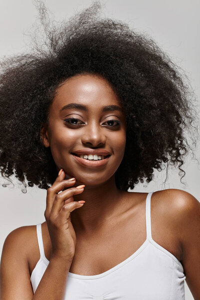 A joyful young African American woman with curly hair smiles brightly in a studio setting.