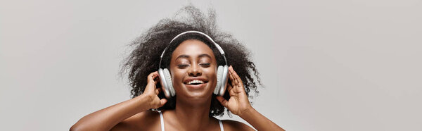 Молодая афроамериканка с кудрявыми волосами в наушниках, потерявшаяся в музыкальных шкафах, слушая.