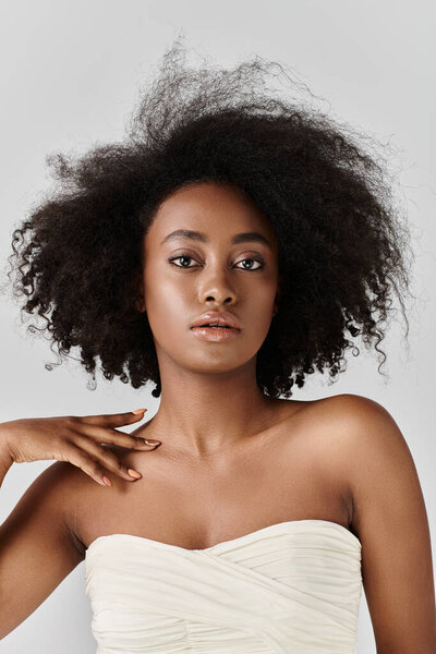Stunning African American woman with curly hair striking a pose in a strapless dress in a studio setting.