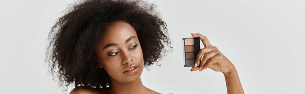 A beautiful young African American woman with curly hair in a studio setting, holding makeup palette
