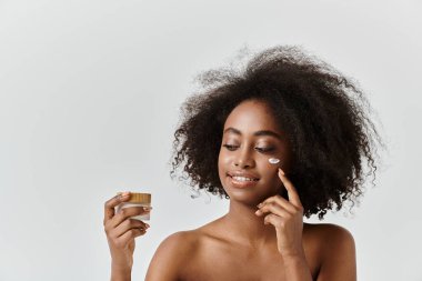 Krema kavanozu tutan kıvırcık saçlı güzel bir Afrikalı Amerikalı kadın.