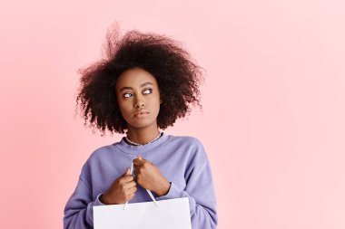 Şık, kıvırcık saçlı, alışveriş çantası tutan, moda ve cazibe gösteren Afro-Amerikan bir bayan..