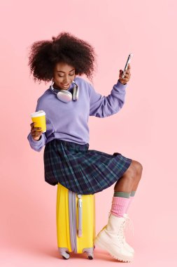 Güzel, kıvırcık saçlı, cep telefonu ekranına dalmış, bir bavulun üzerinde oturan Afro-Amerikan bir kadın..