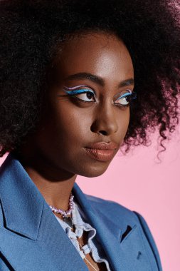Şık, kıvırcık saçlı, takım elbiseli ve büyüleyici mavi makyajlı Afro-Amerikan bir kadın..
