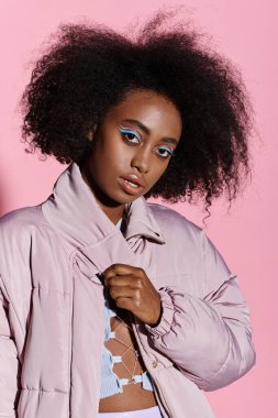 Kıvırcık saçlı, canlı pembe arka planda poz veren şık Afrikalı Amerikalı kadın..