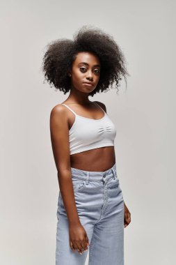A stylish African American woman with curly hair wearing a crop top and jeans. clipart