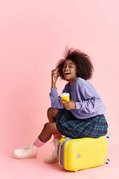 一位衣着时髦 一头卷发的年轻非洲裔美国女人在手提箱上放松了下来 一边品尝着一杯咖啡 — 图库照片