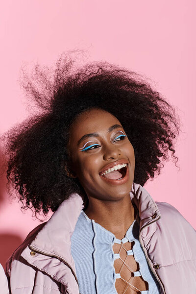 A stylish young African American woman with curly hair smiles brightly in a studio setting, exuding confidence and joy.