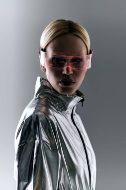 extravagant woman with sci fi glasses in robotic silver clothing looking at camera on gray backdrop clipart
