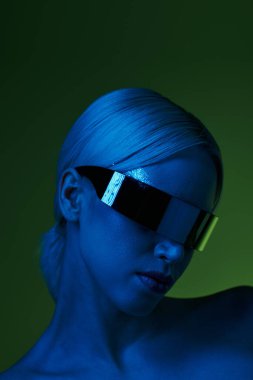 extravagant blonde woman with sci fi robotic sunglasses posing in blue lights on green backdrop clipart