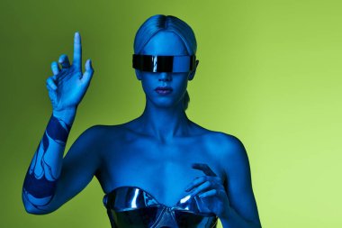 Gümüş renkli robotik elbiseli, bilim kurgu güneş gözlüklü yeşil fonda poz veren müsrif bir kadın.