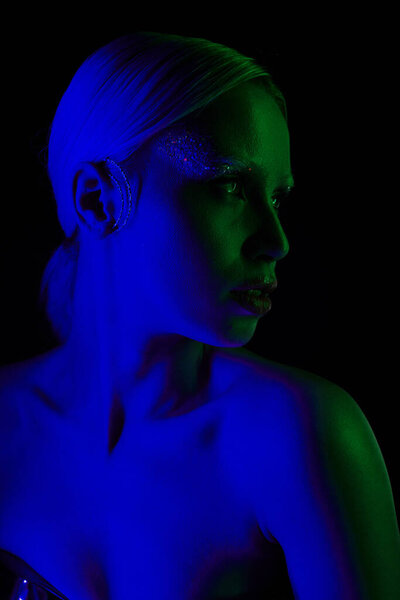 beautiful futuristic woman in metallic sci fi clothing posing in blue lights and looking away