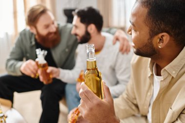 Three cheerful, interracial men in casual attire sitting around a table, bonding over beers and enjoying a good time together. clipart