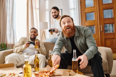 Üç neşeli, yakışıklı, ırklar arası giyinmiş, masanın etrafında oturmuş, mutlu bir şekilde pizza yiyorlar..