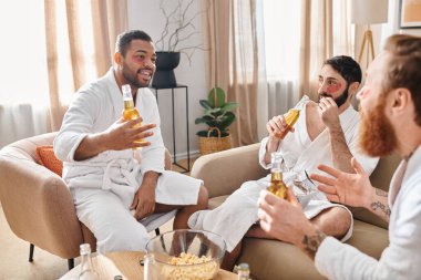 Three diverse cheerful men in bathrobes relax and have a great time together, sitting on top of a couch. clipart