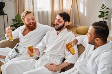 Three diverse, cheerful men in bathrobes enjoying a great time together while sitting on top of a couch. clipart