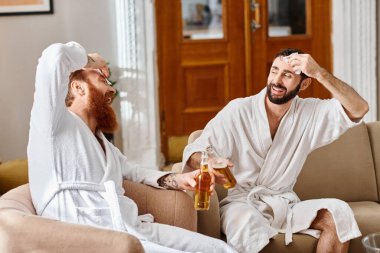 İki adam kanepede oturuyor, birlikte bira içmekten zevk alırken gülümsüyor ve rahatlıyorlar..