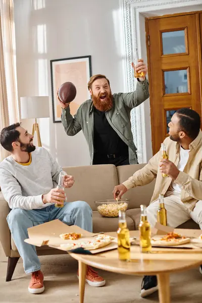 Farklı ırktan üç neşeli, yakışıklı adam gündelik giysiler içinde bir kanepede otururken birbirlerine eşlik ederek eğleniyorlar..