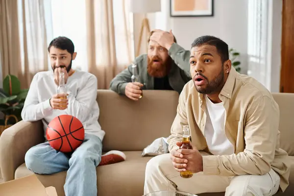 stock image Three cheerful, interracial men in casual attire sit and lounge on a sofa, exuding camaraderie and friendship.