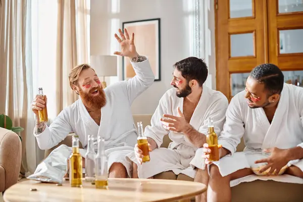 バスローブの3人の多様な男性がテーブルの周りに集まり 飲み物を共有しながらお互いを楽しんでいます — ストック写真