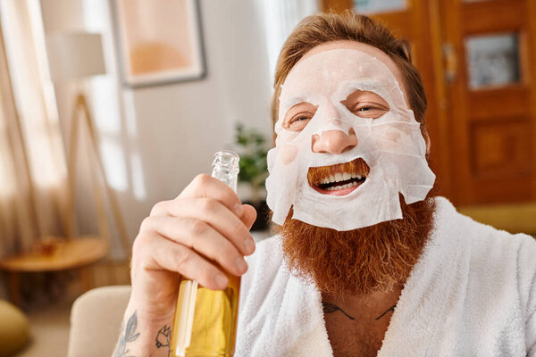A man in a facial mask holds a bottle of bear and smiling happily.