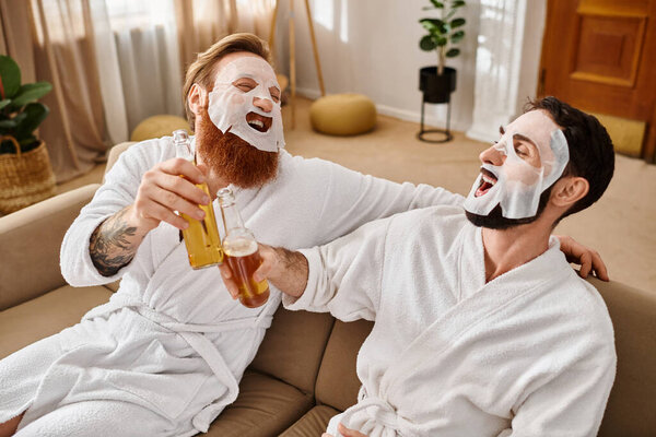 Two cheerful men in bathrobes relax on a couch, enjoying each others company and camaraderie.
