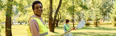 Diverse couple in a bright yellow vests cleaning in a park. clipart