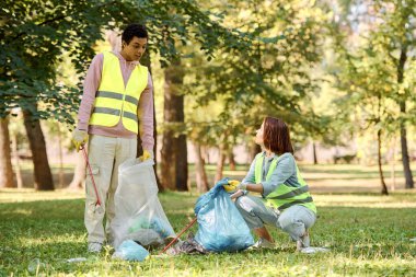 Güvenlik yelekleri ve eldivenleriyle parkı birlikte temizleyen sosyal olarak aktif bir çift..