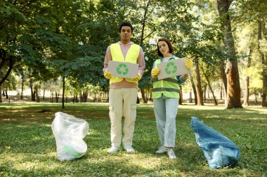 A diverse couple in safety vests and gloves stand in the grass, cleaning the park together, embodying love and environmental responsibility. clipart