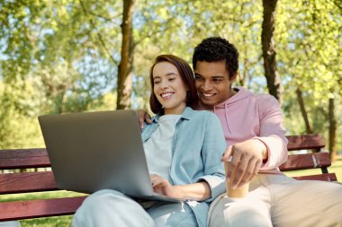 A stylish couple, dressed vibrantly, immersed in a laptop in a park bench. clipart