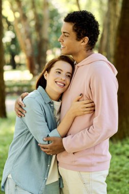 Canlı giyinmiş bir adam parkta bir kadını nazikçe kucaklıyor, doğal bir ortamda bir yakınlık ve bağlantı anı sergiliyor..