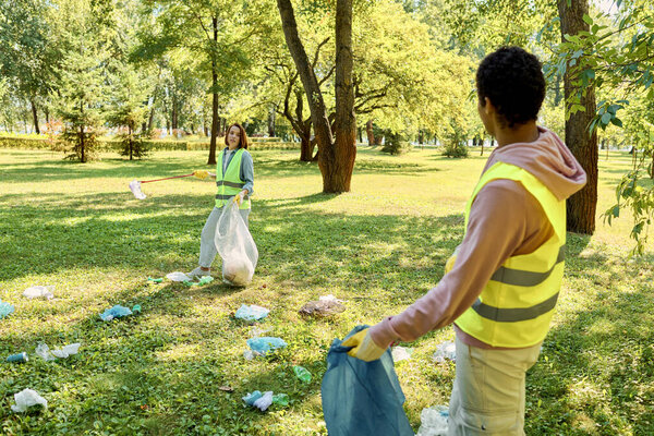 A socially active couple in safety vests and gloves stands in the grass, cleaning the park together with love and care.