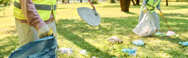 Diverse couple in safety vests cleaning park together.